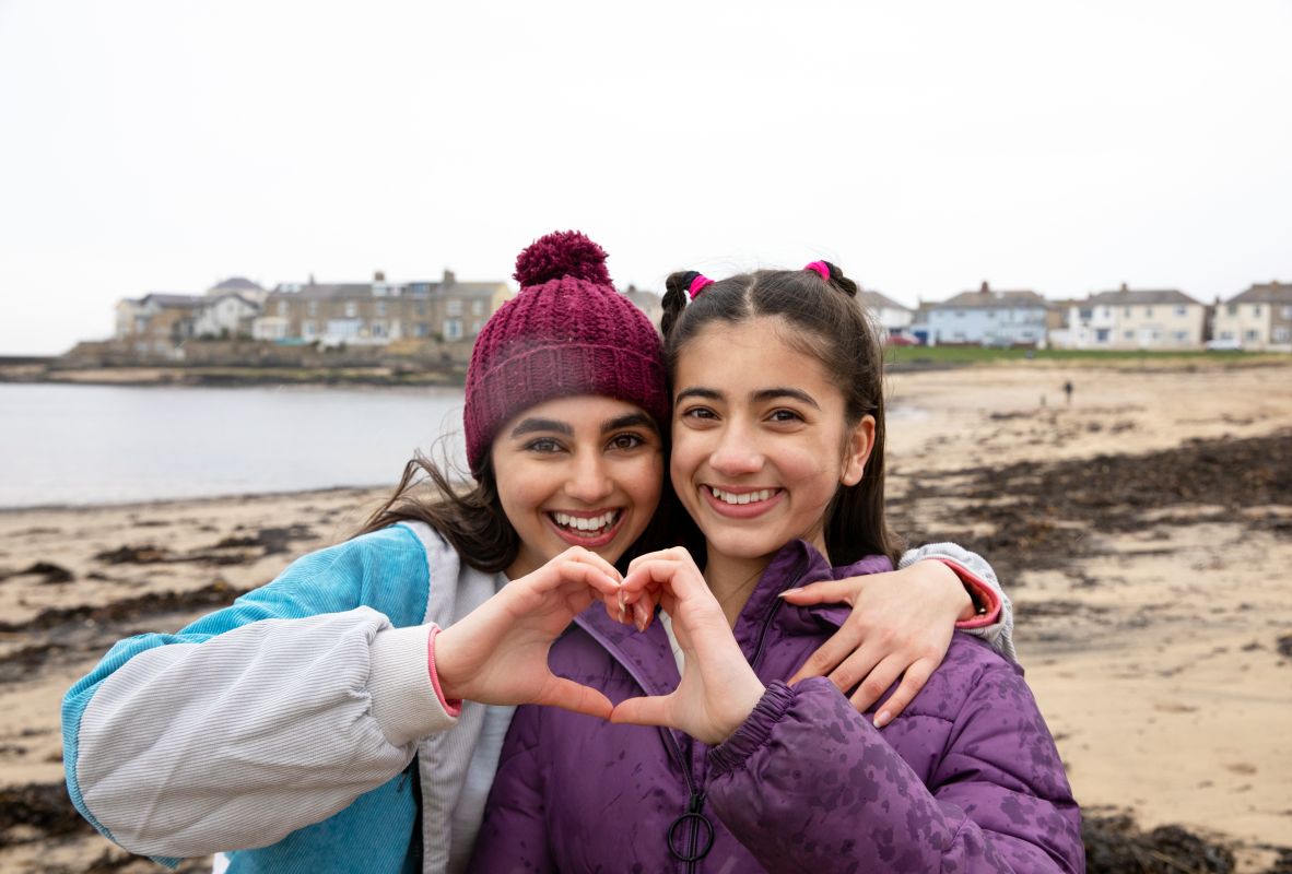 Image of two sisters embracing forming a heart shape together with their hands