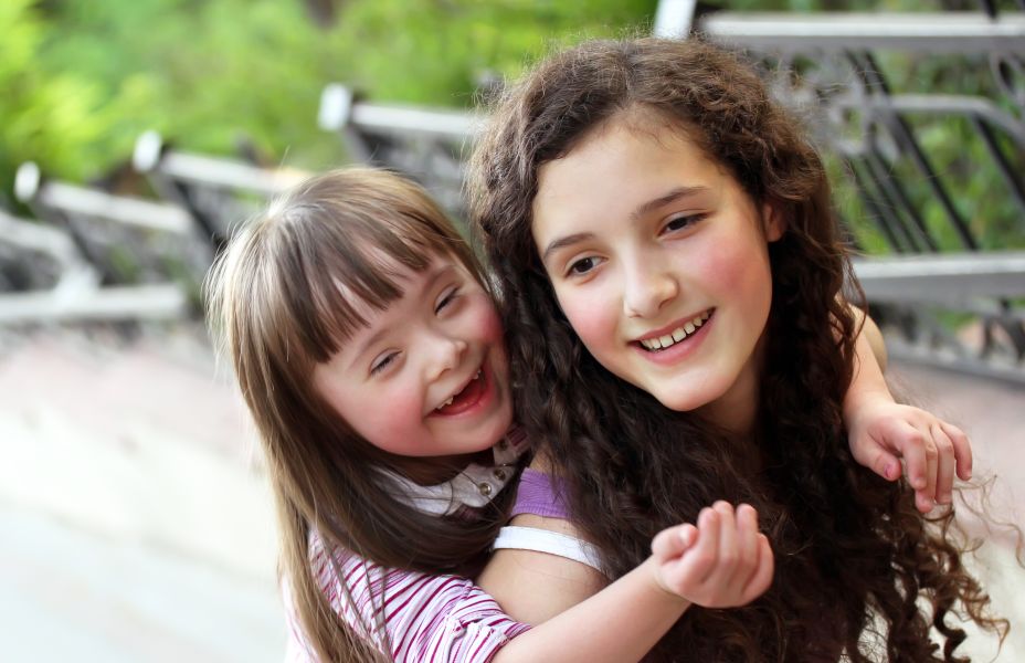 young girl giving her sister who has downs syndrome a piggy back carry