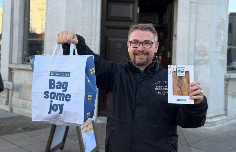 smiling man holding a Greggs bag of sausage rolls