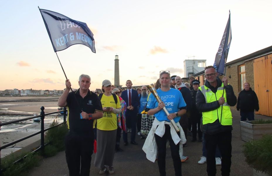 woman in blue T shirt carries a baton to symbolise hope in a crowd of people with Margate sea in the background